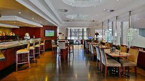 Un amplio vestíbulo de hotel con zona de bar, diversas opciones de asientos y grandes ventanales que permiten la entrada de luz natural.