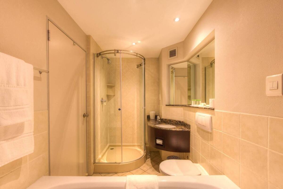 Une salle de bain dotée d’une douche à parois de verre, d’un lavabo avec un plan de toilette en marbre, de toilettes et d’une grande baignoire.