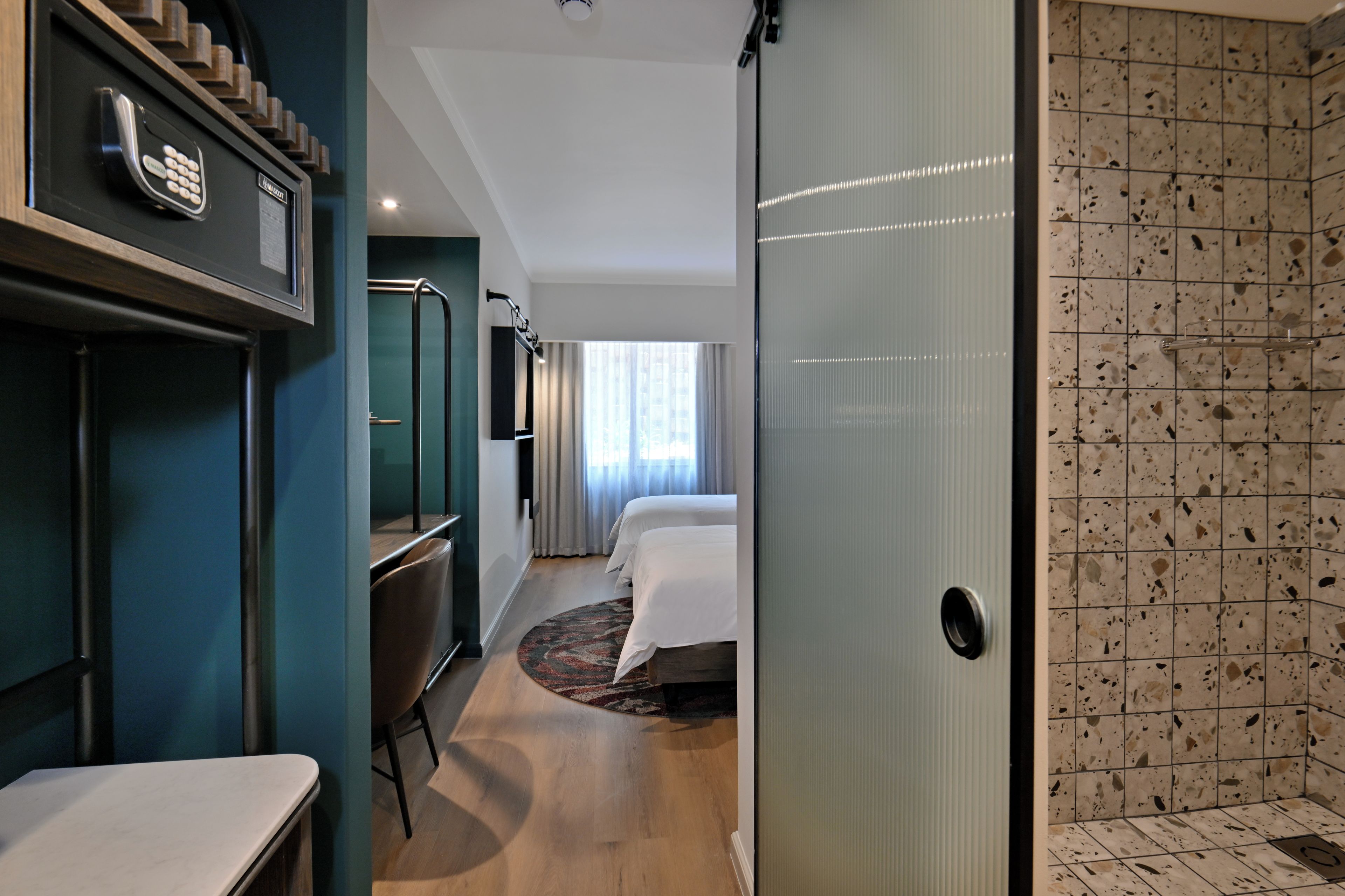 Habitación de hotel con cama, escritorio, silla, baño con ducha y puerta con cerradura de tarjeta.