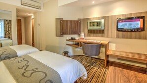 A hotel room with two beds, a desk, a chair, a TV, and a wooden accent wall.