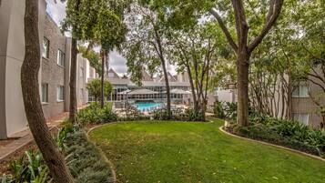 Un patio con piscina, rodeado de árboles y un césped bien cuidado.