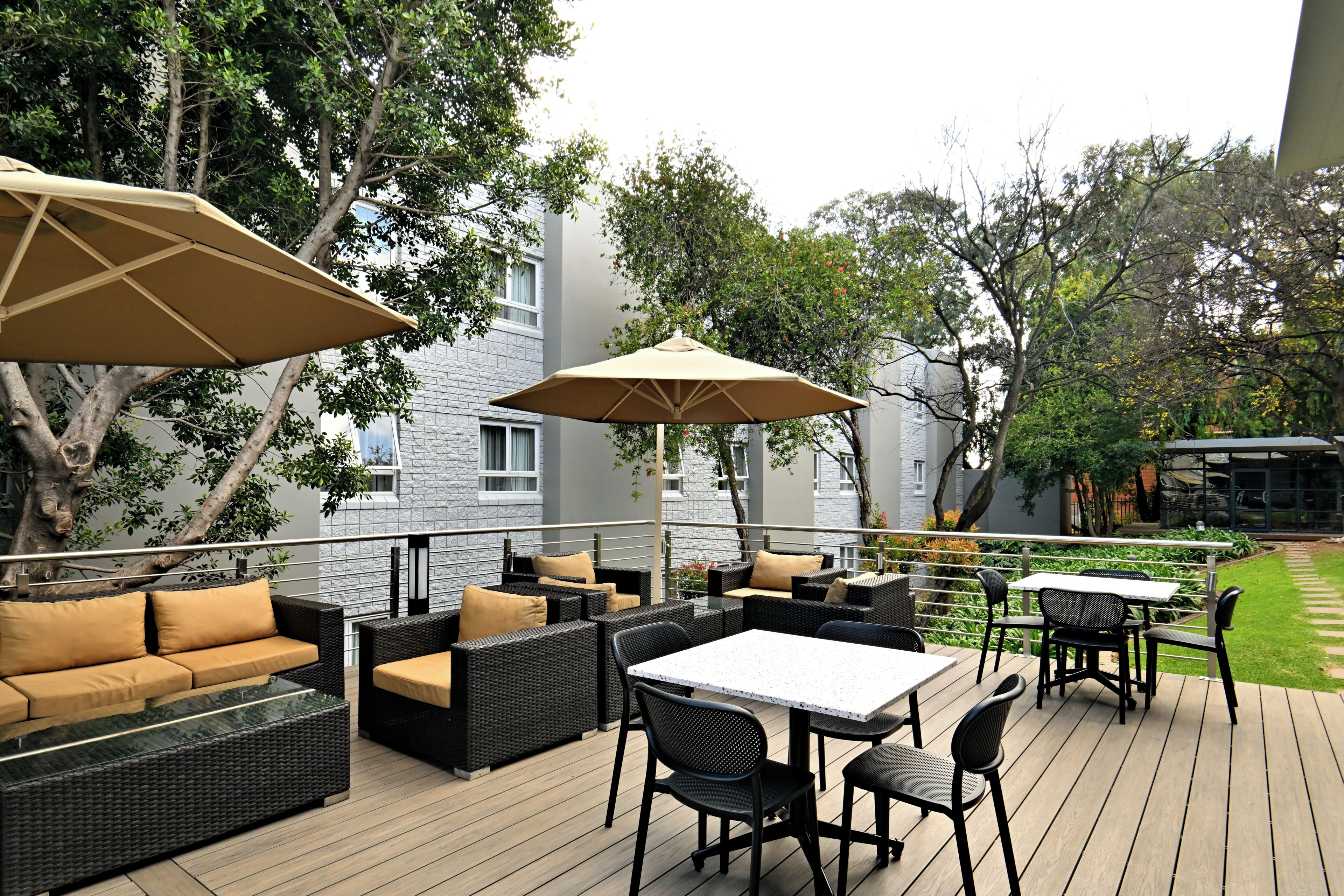 Une terrasse extérieure avec des meubles en osier, une table blanche et un grand parasol.