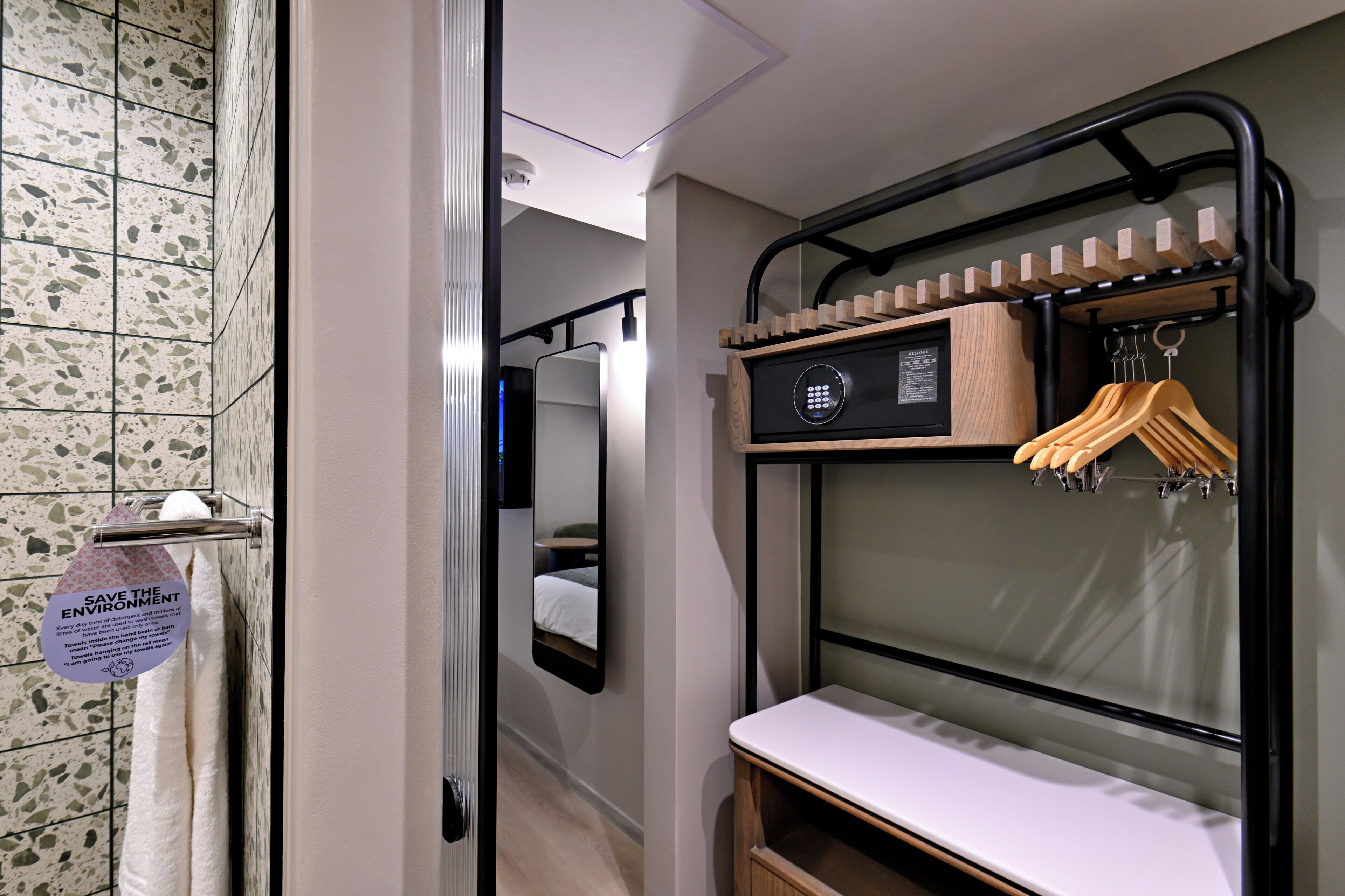 Una habitación de hotel compacta con un armario con espejo, un perchero y una mesita de noche pequeña.