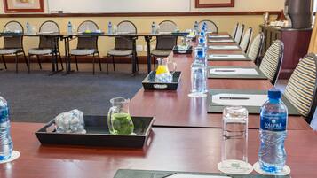 A conference room with long tables, chairs, water bottles, and a pitcher of green tea.