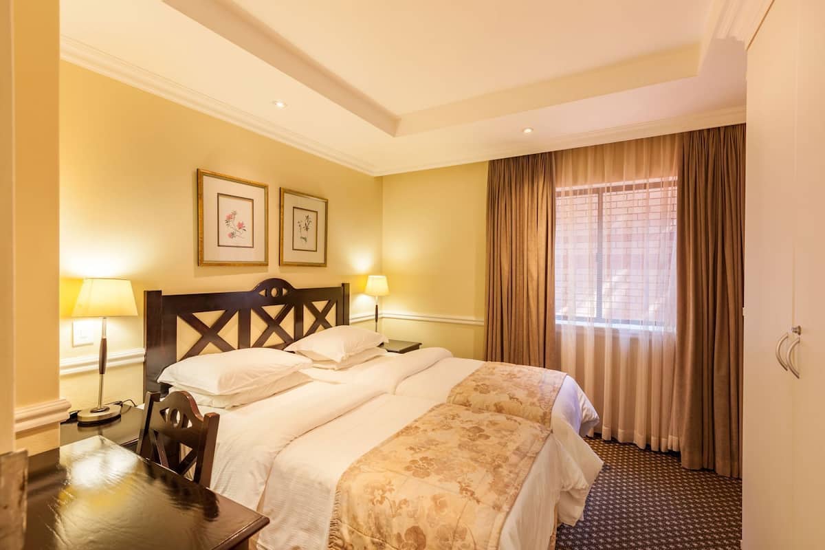A hotel room with a bed, two bedside lamps, a desk, and a window with curtains.