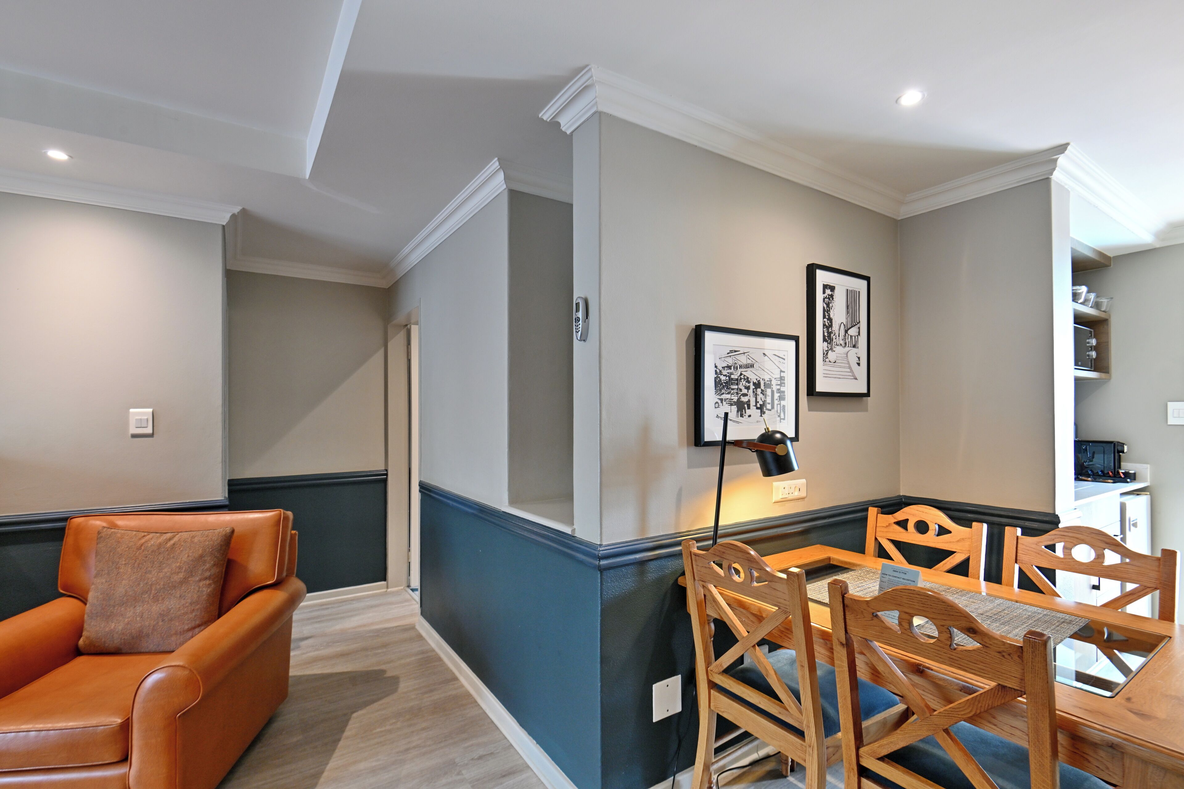 Un coin repas avec une table et des chaises en bois, un canapé en cuir marron et des œuvres d’art encadrées accrochées au mur.