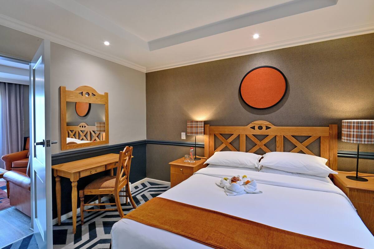 A hotel room with a bed, a desk, a chair, a mirror, and a round wall decoration.