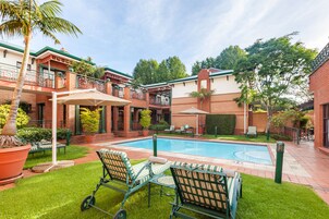 Zona de piscina con sillones de descanso, una palmera y un edificio de ladrillo con balcón.