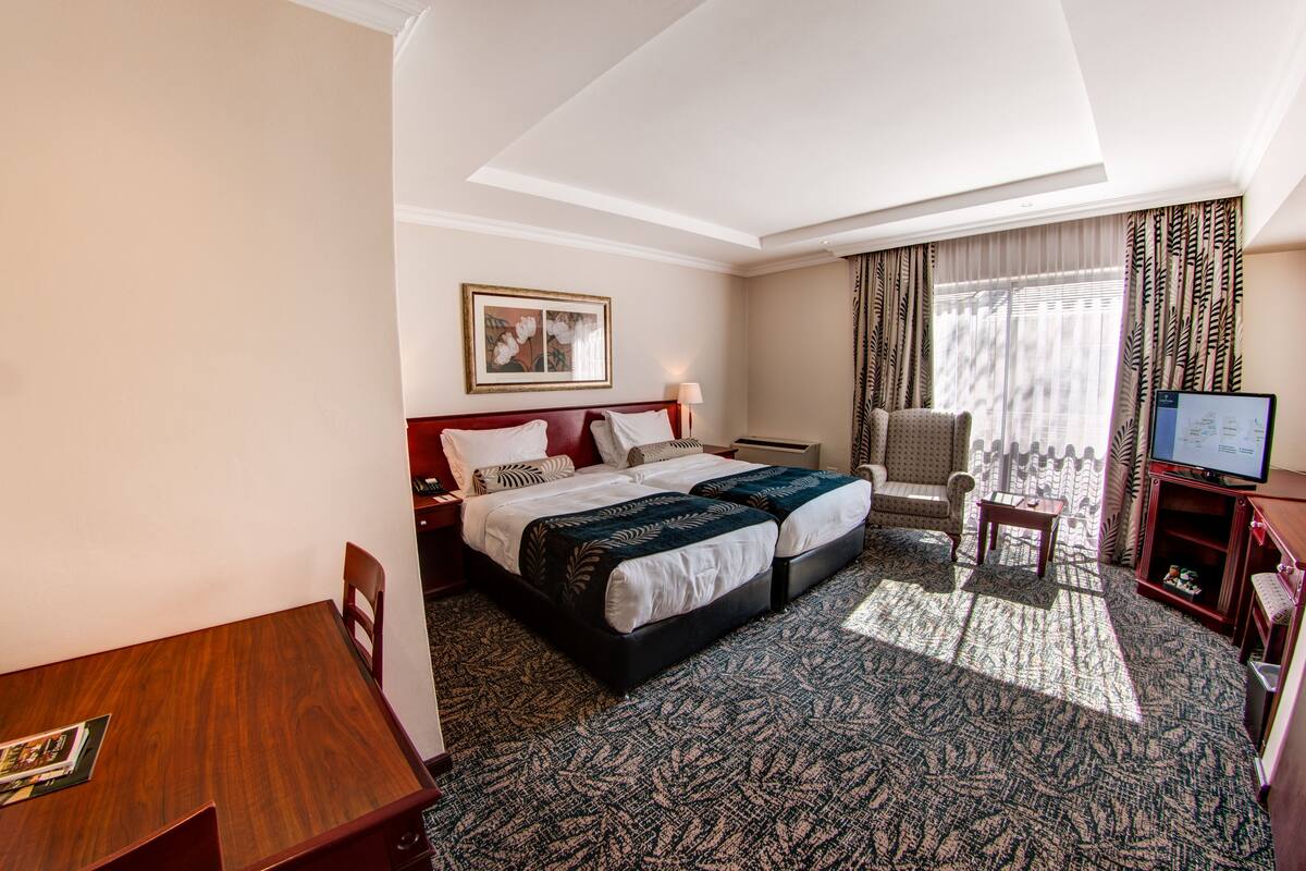 Een hotelkamer met een tweepersoonsbed, een bureau, een stoel, een televisie en een raam met gordijnen.