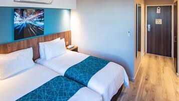 Une chambre d’hôtel avec deux lits, une tête de lit en bois, un climatiseur fixé au mur, une table de chevet et une porte avec une pancarte.