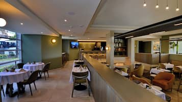 Um restaurante com mesas, cadeiras, um bar e uma televisão.