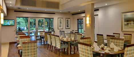 A dining area with multiple tables and chairs, large windows, and framed artwork on the walls.