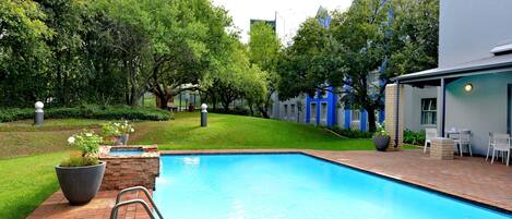 A swimming pool with a brick deck, surrounded by trees and a building with blue accents.