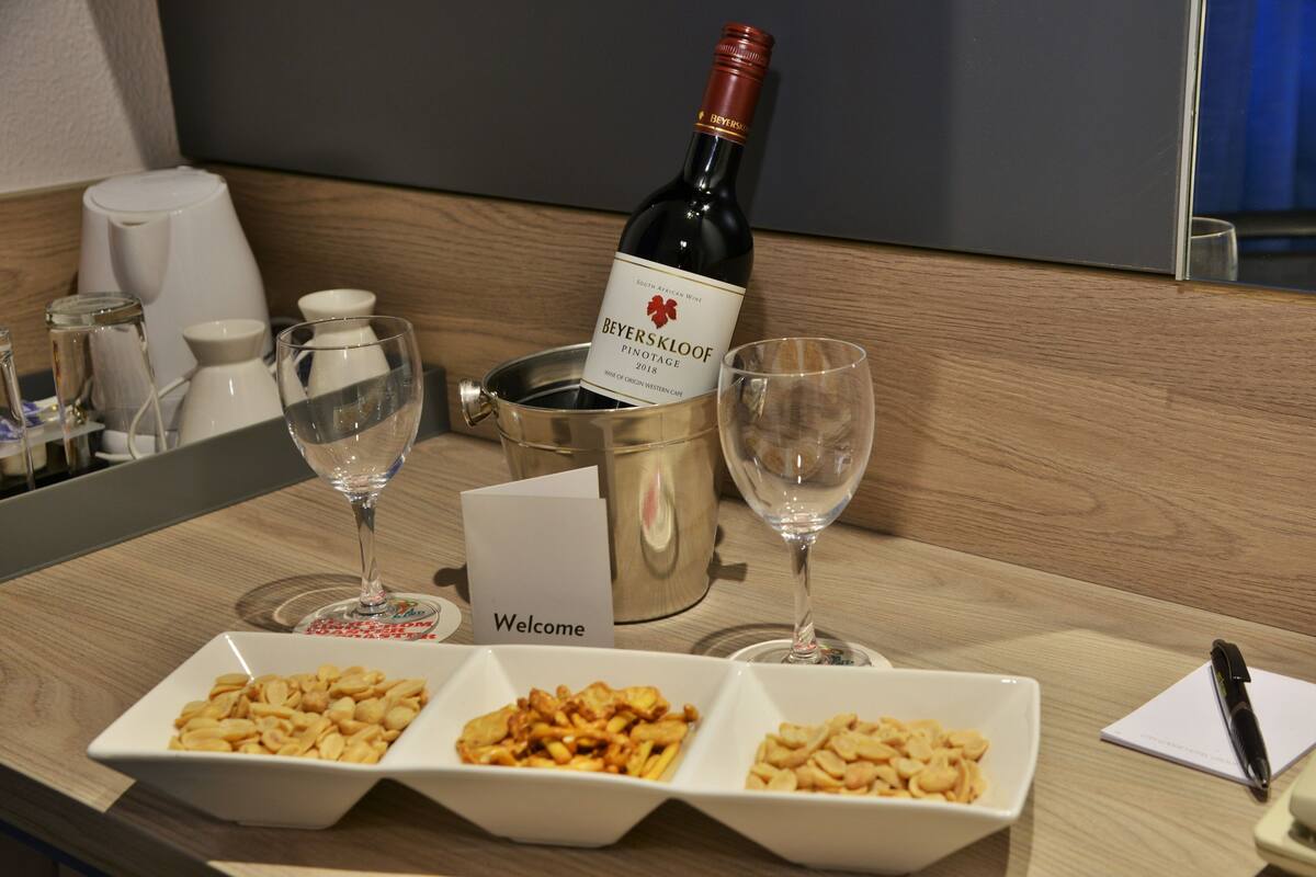 A hotel reception area with a bottle of Beyerskloof Pinotage 2018 wine, three glasses, and a welcome card.