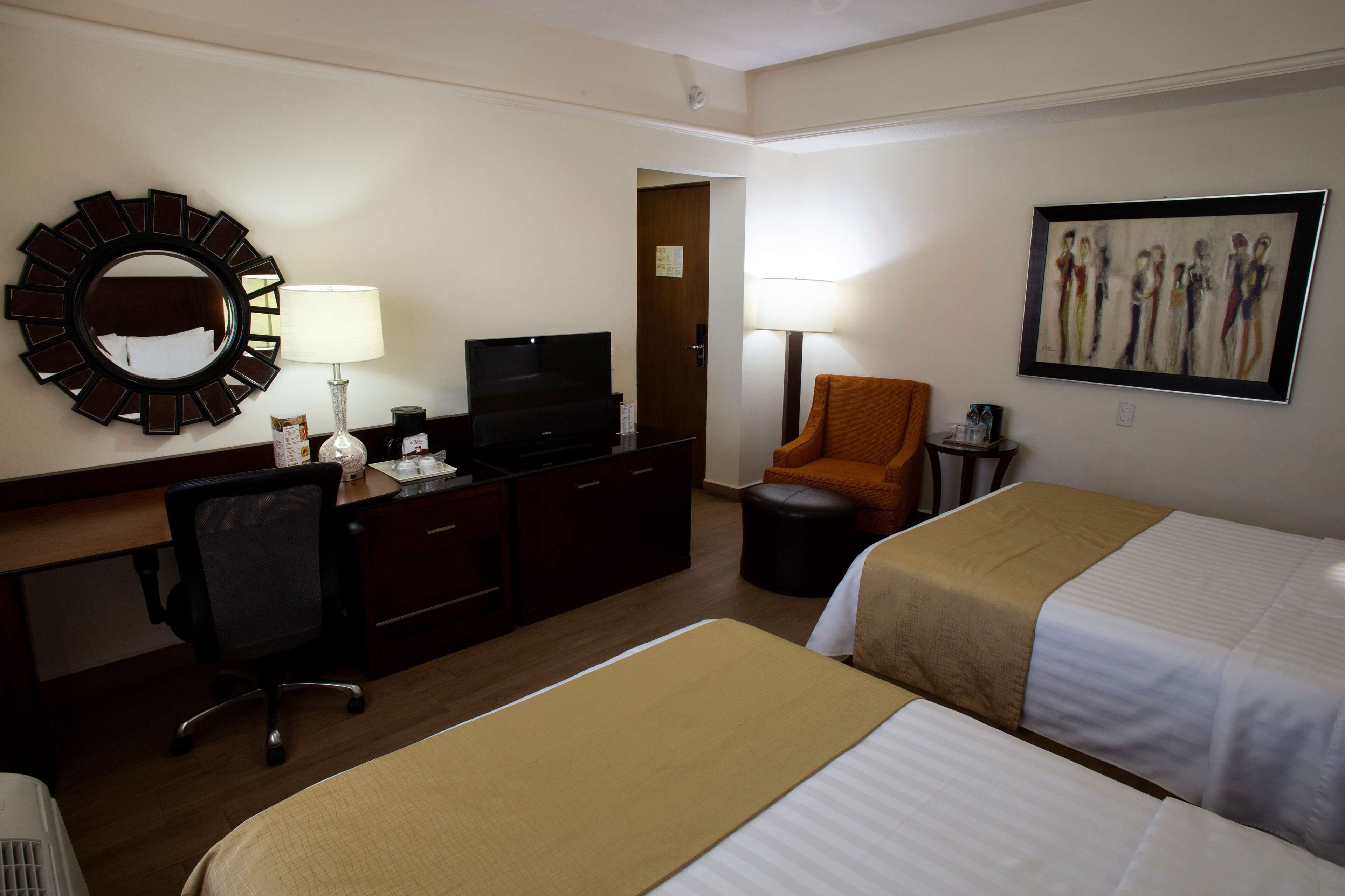 A hotel room with two beds, a desk with a computer, a chair, a TV, and a painting on the wall.