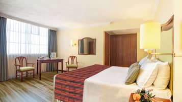 A hotel room with a bed, a desk, two chairs, a mirror, and a lamp.