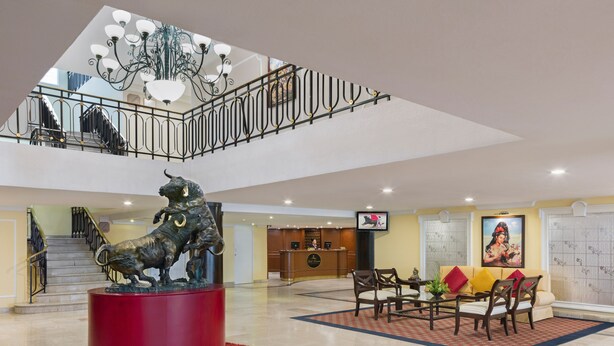 A spacious lobby with a red cylindrical sculpture, a reception desk, a seating area with chairs, a staircase, and a chandelier. - Francia Aguascalientes (Aguascalientes)