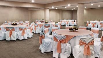 A large conference room with multiple round tables, each covered with white tablecloths and adorned with peach-colored sashes.