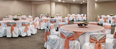 A large conference room with multiple round tables, each covered with white tablecloths and adorned with peach-colored sashes.
