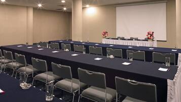 A conference room with a long table, chairs, a projector screen, and a flower arrangement.