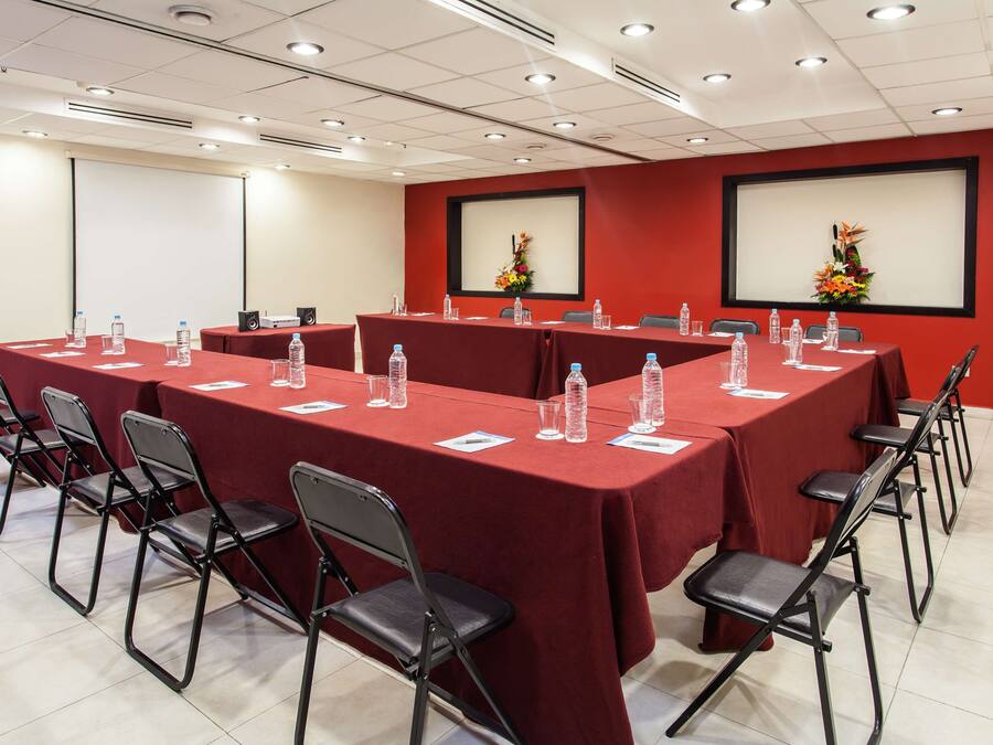 A conference room with red tablecloths, foldable chairs, water bottles, and a projector.