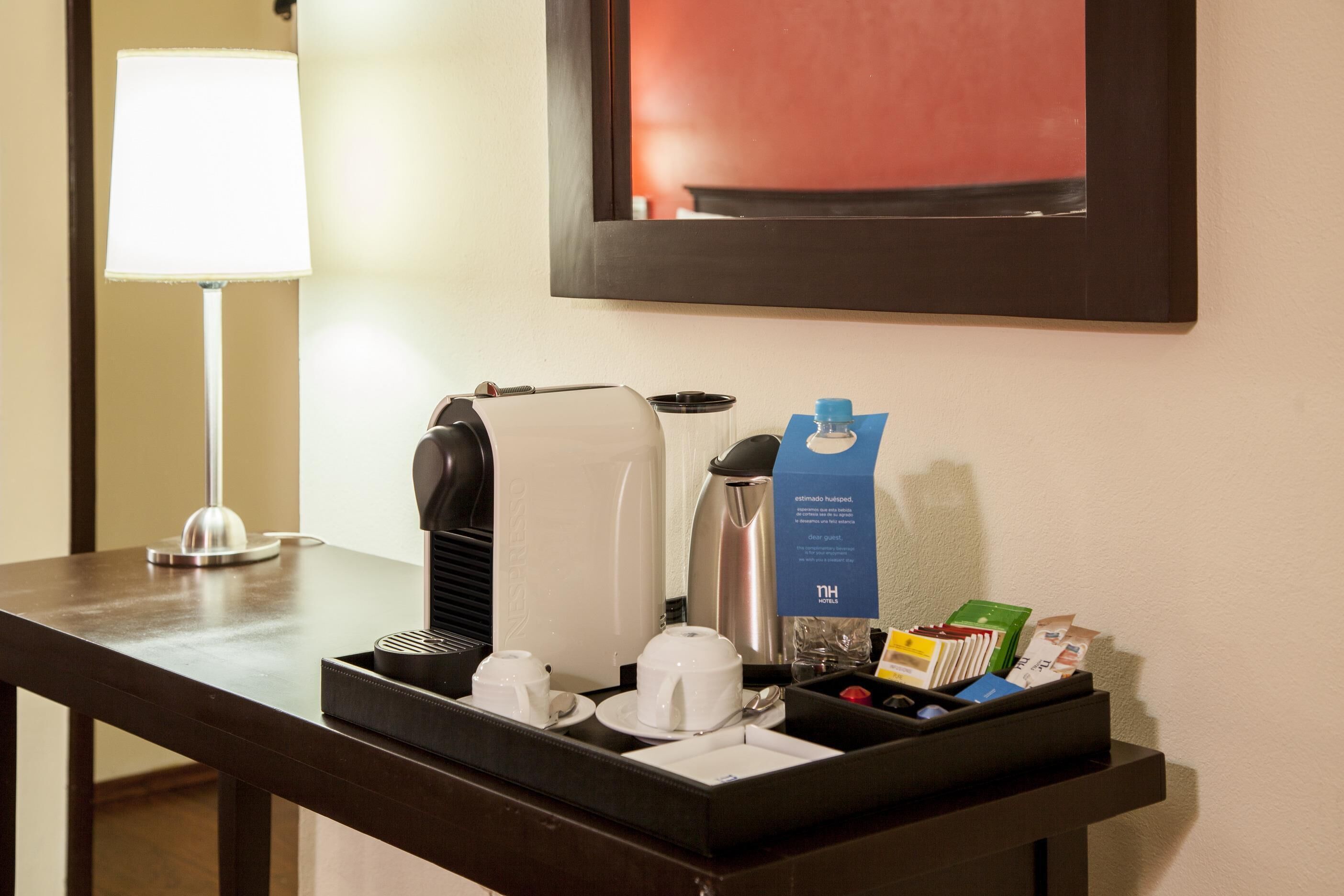 Angolo colazione in camera con macchina del caffè, teiera, tazze e vassoio con condimenti e menu.