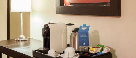 Angolo colazione in camera con macchina del caffè, teiera, tazze e vassoio con condimenti e menu.