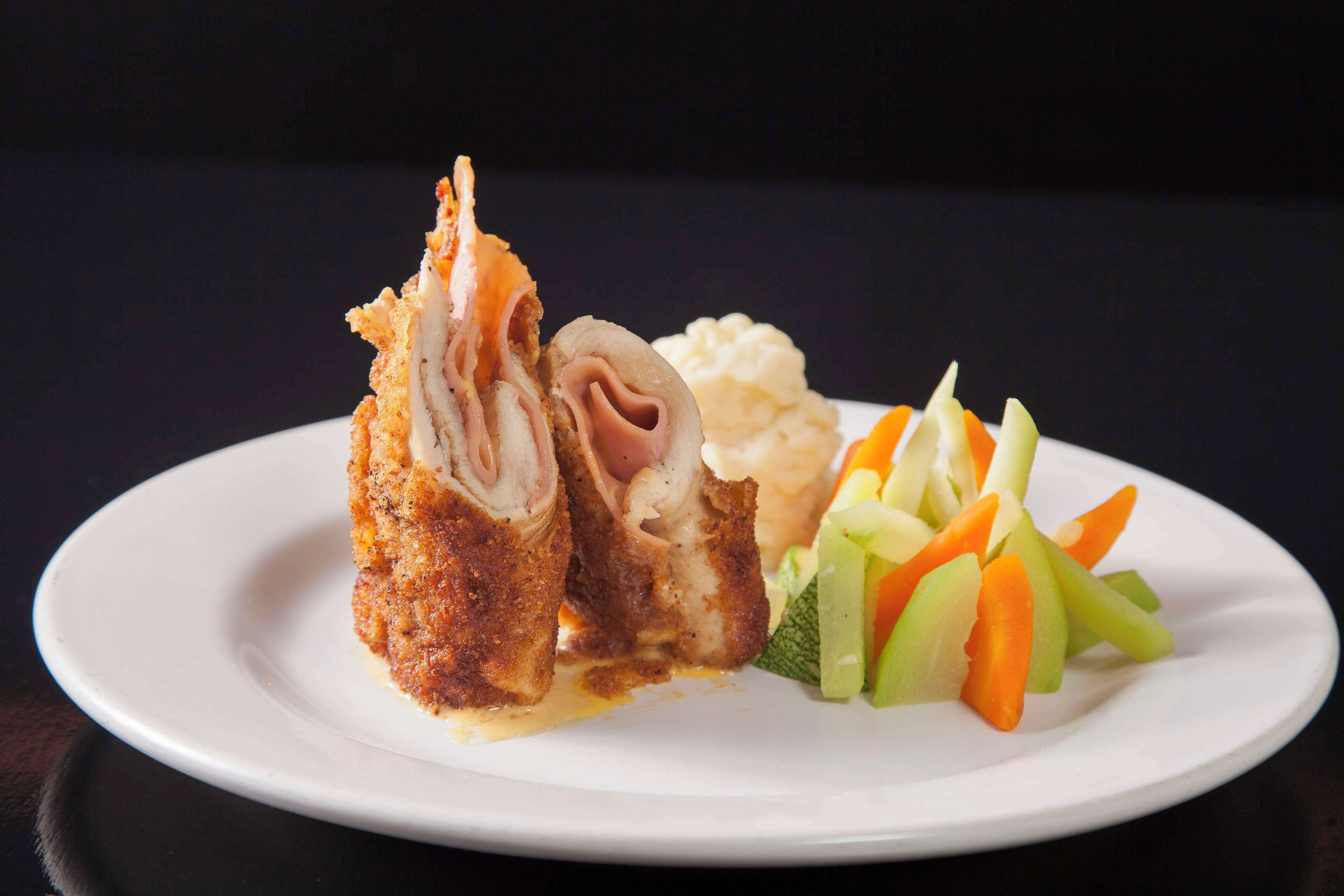 Un plato con una milanesa, puré de papas y una guarnición de vegetales en rodajas.