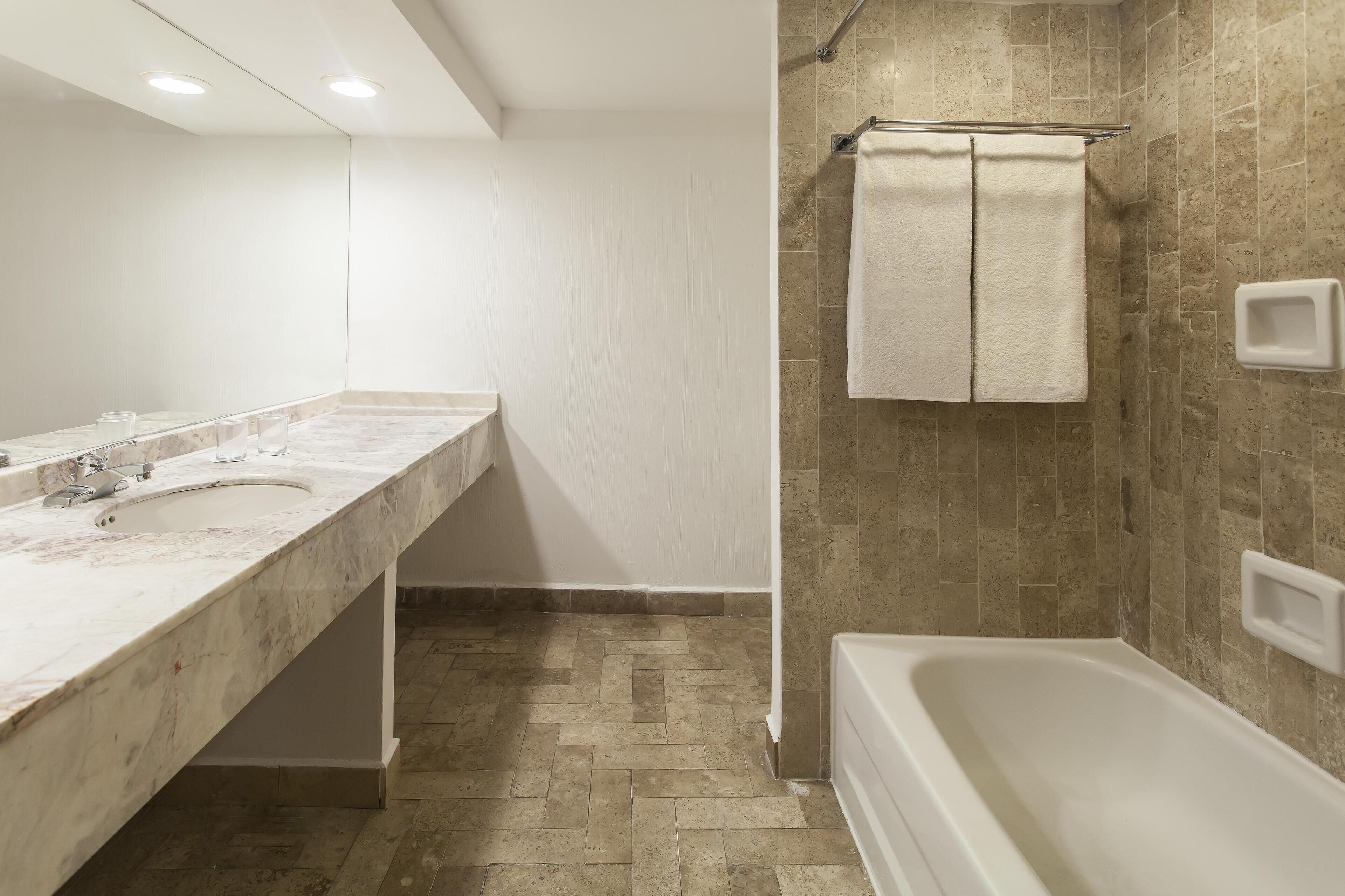 Un baño con lavamanos de mármol, bañera y zona de ducha con azulejos color beige.