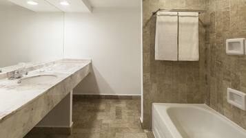 Un baño con lavamanos de mármol, bañera y zona de ducha con azulejos color beige.
