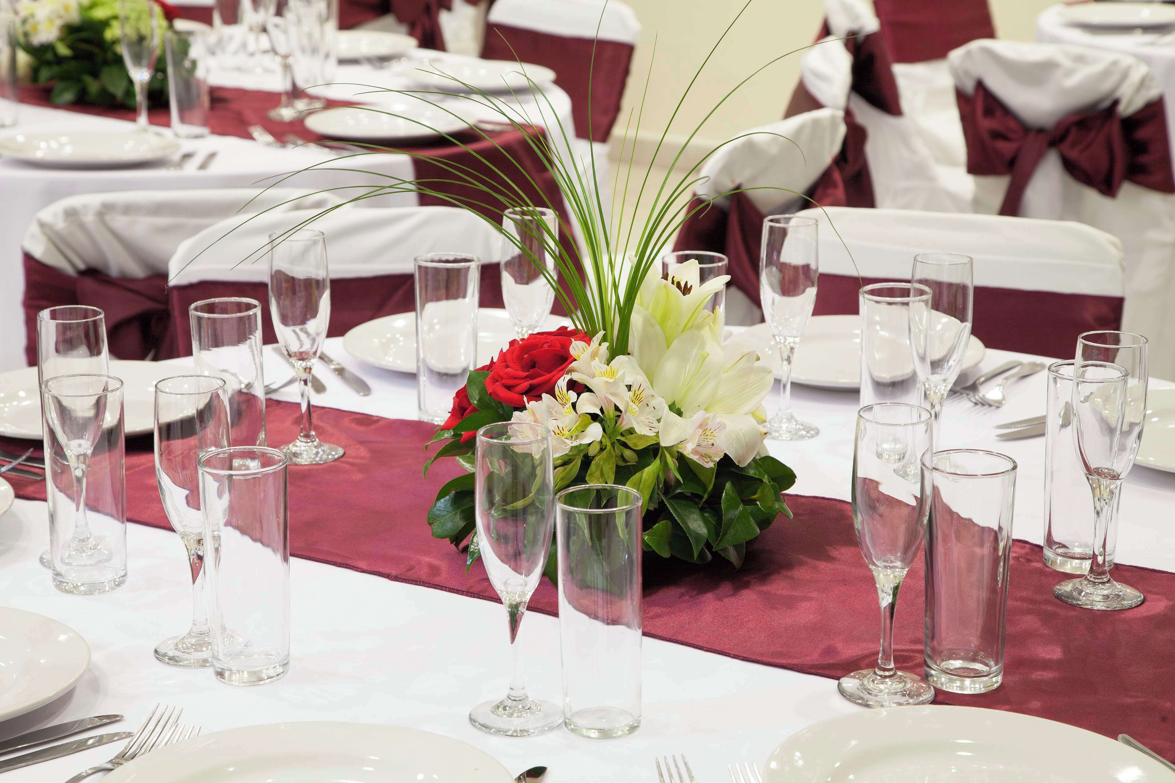 A table set for a formal event with clear glassware, white plates, and a centerpiece of red and white flowers.