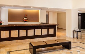 Un área de recepción con mostrador de mármol, una banca y un arreglo floral en la pared.
