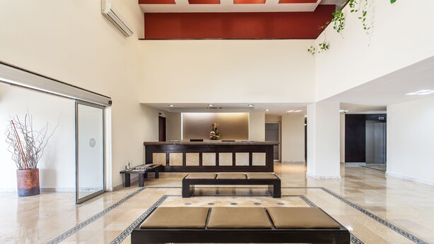 Un hall amplio con una zona de estar central, una recepción y un diseño moderno con suelo de mármol y techo alto.