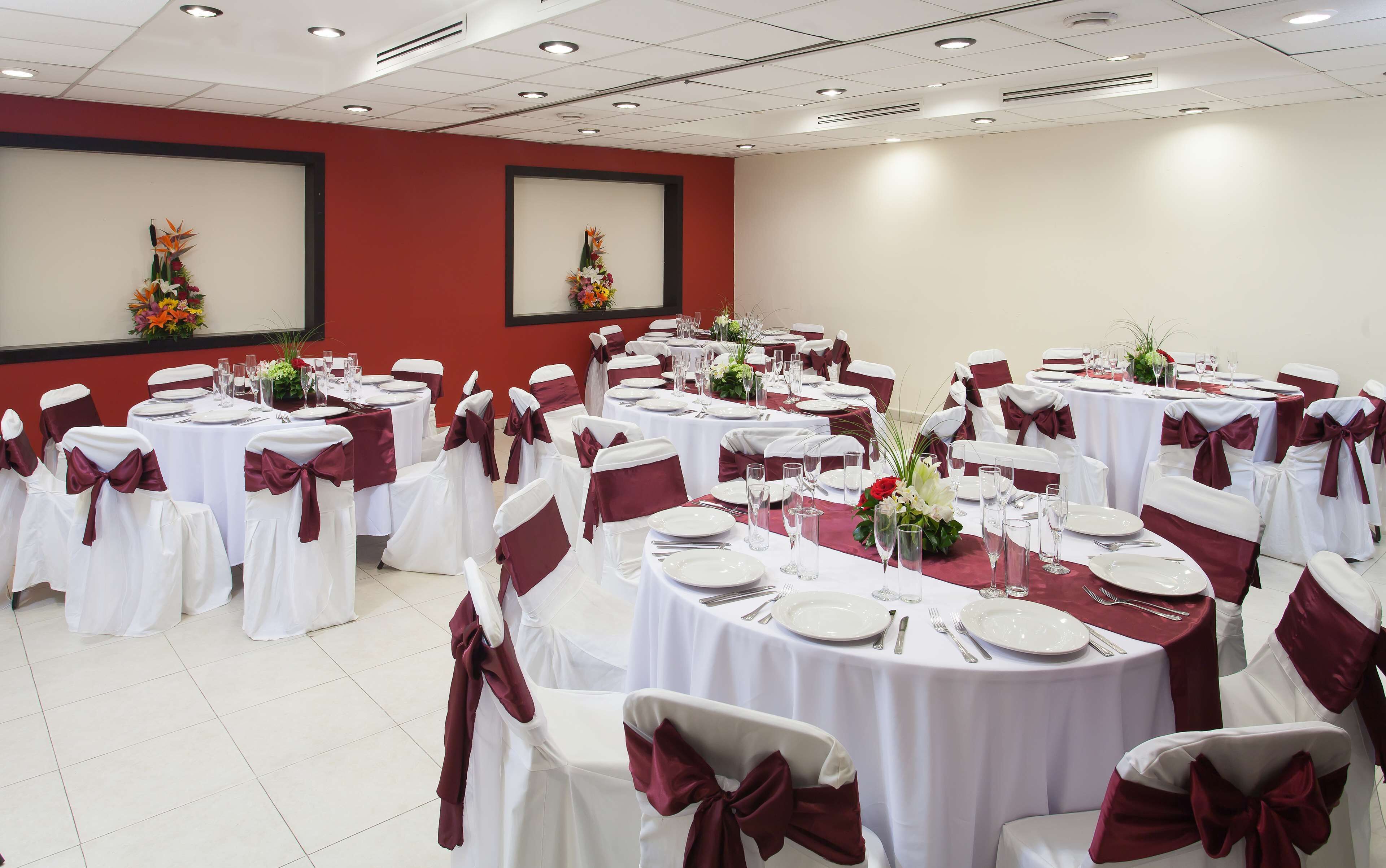 A banquet hall with round tables, white tablecloths, and chairs with red sashes.