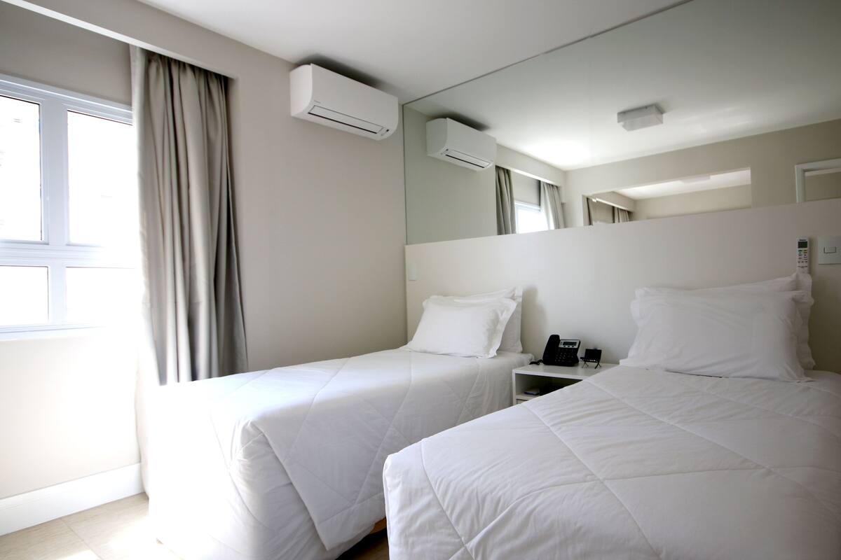 Une chambre d’hôtel avec deux lits simples, une table de chevet avec un téléphone et un appareil de climatisation fixé au mur.