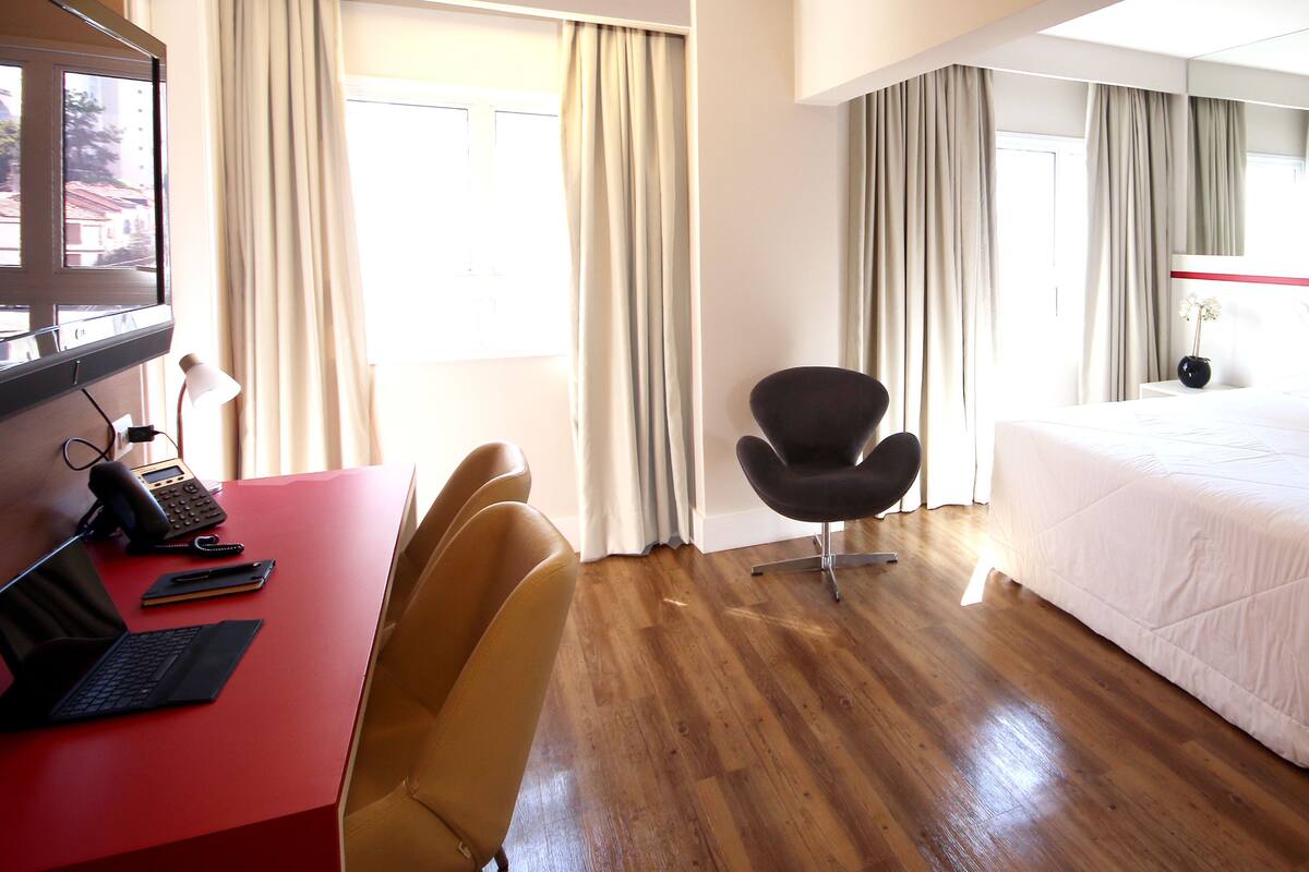 Une chambre d’hôtel avec un lit, un bureau avec un ordinateur portable, une chaise et un téléviseur.
