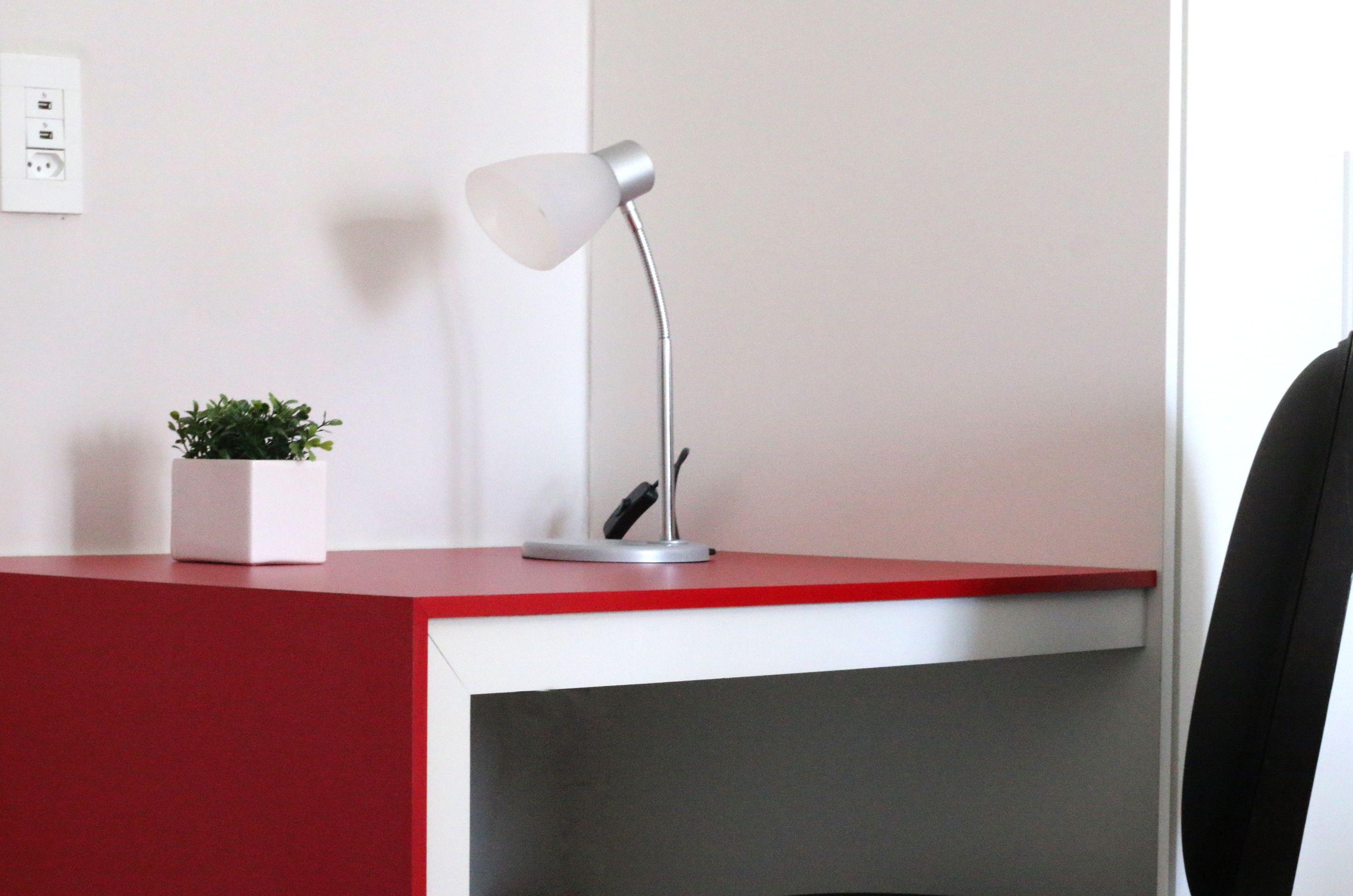 A desk with a modern lamp, a small potted plant, and a red and white desk surface.