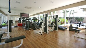 Een sportschool met diverse fitnessapparaten, een televisie en grote ramen met uitzicht op het buitenland.