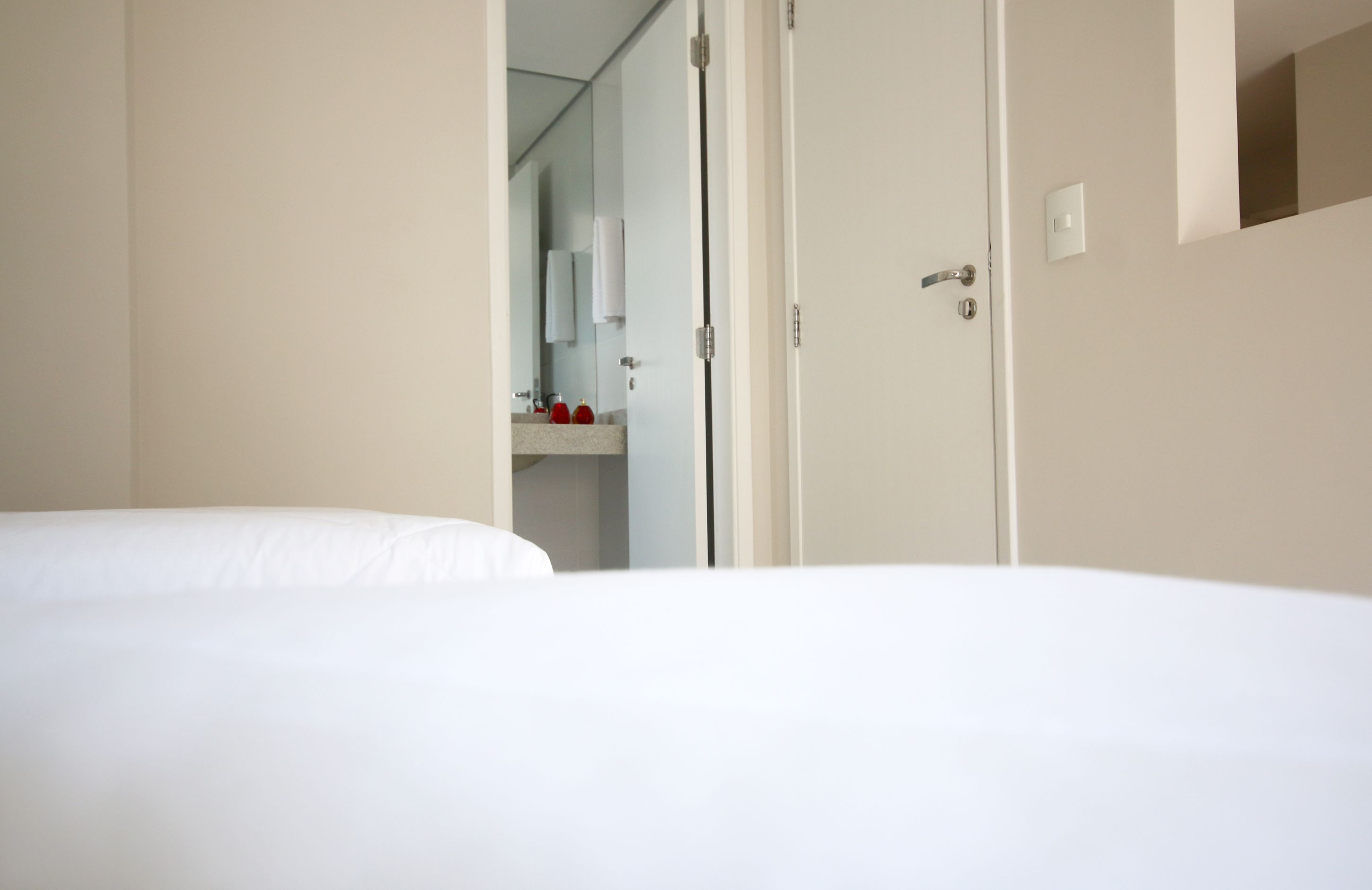 A hotel room with a bed, a bathroom with a mirror, and a door.