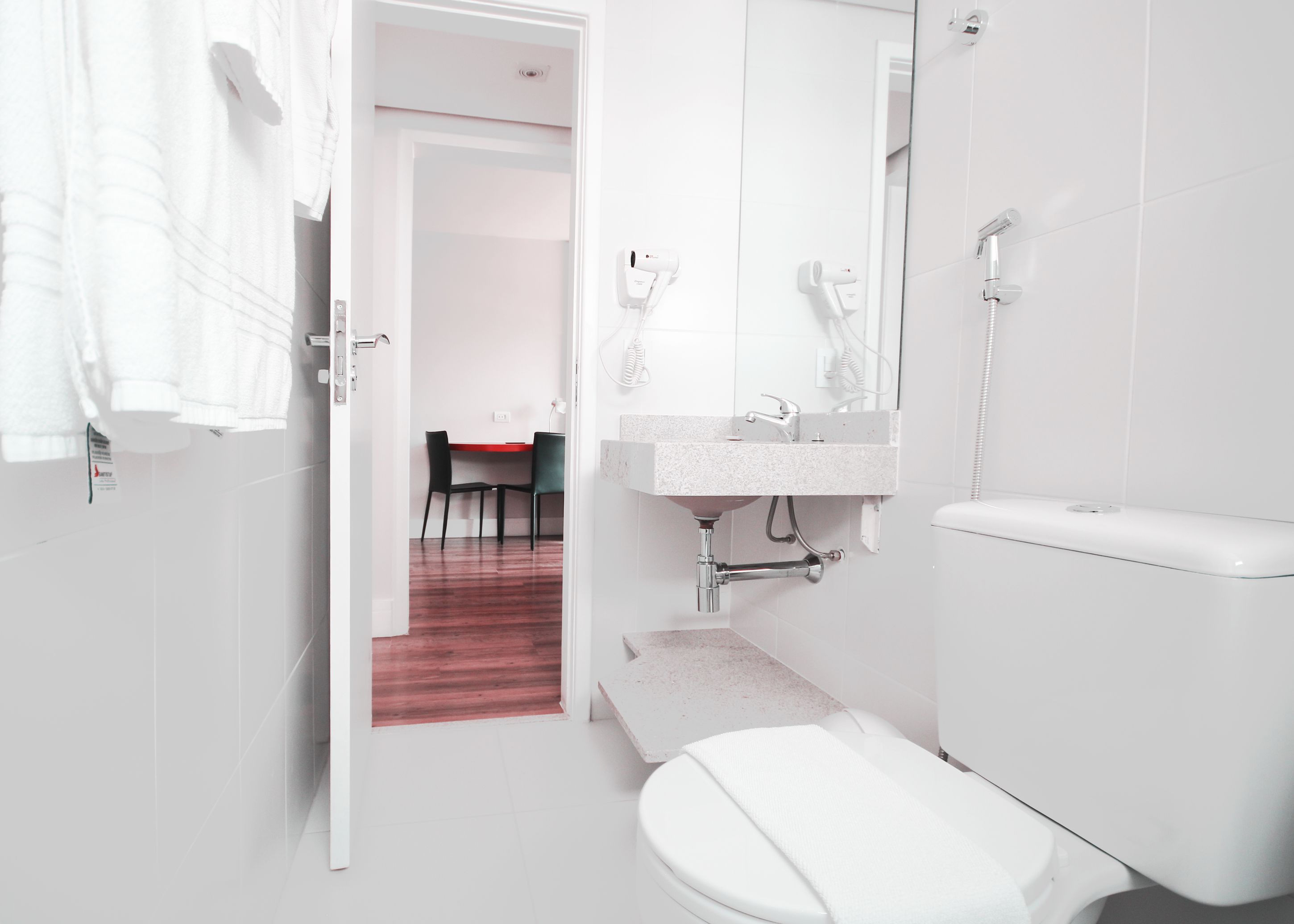 A modern bathroom with a toilet, sink, and shower. A red carpet leads to a dining area with a table and chairs.