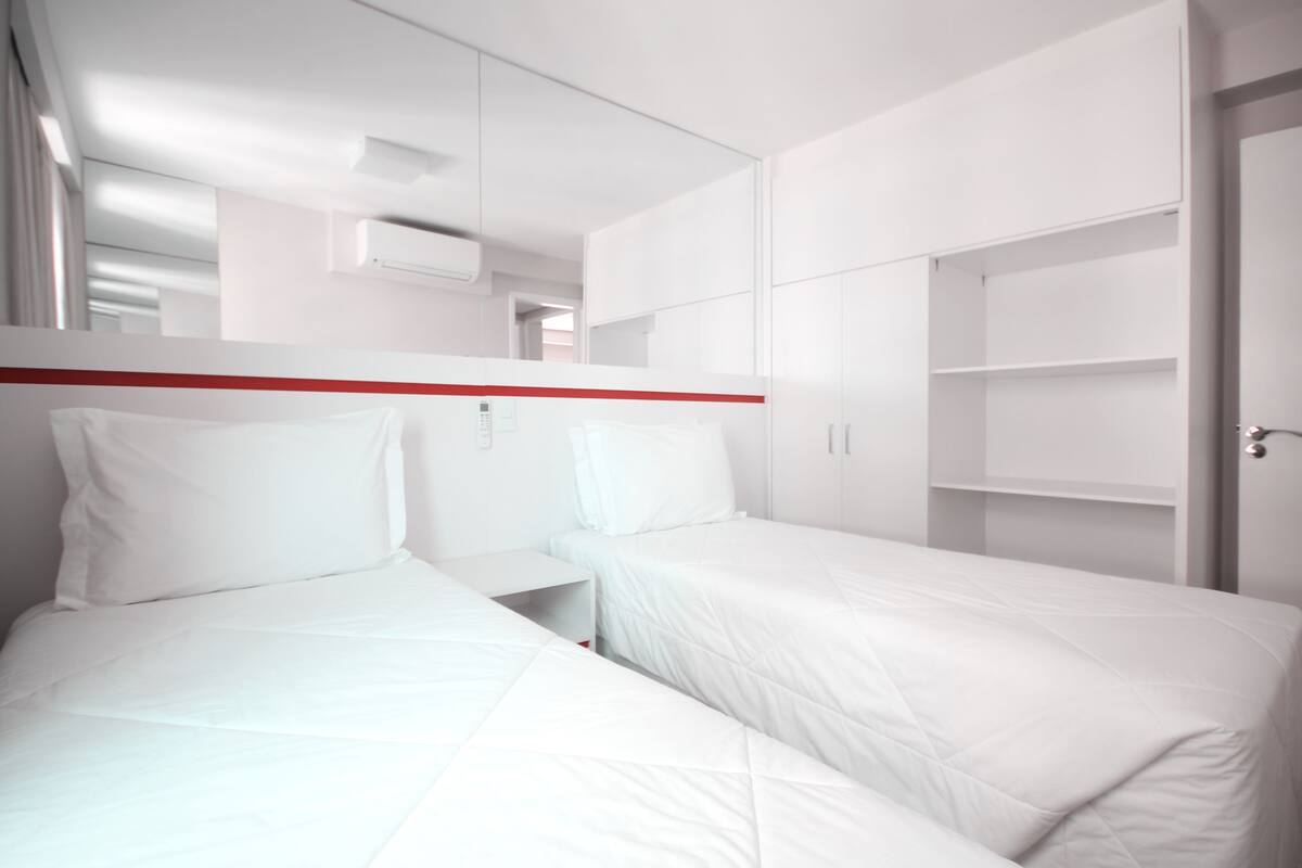 Une chambre d’hôtel moderne avec deux lits, un mur d’accent rouge et des armoires intégrées.