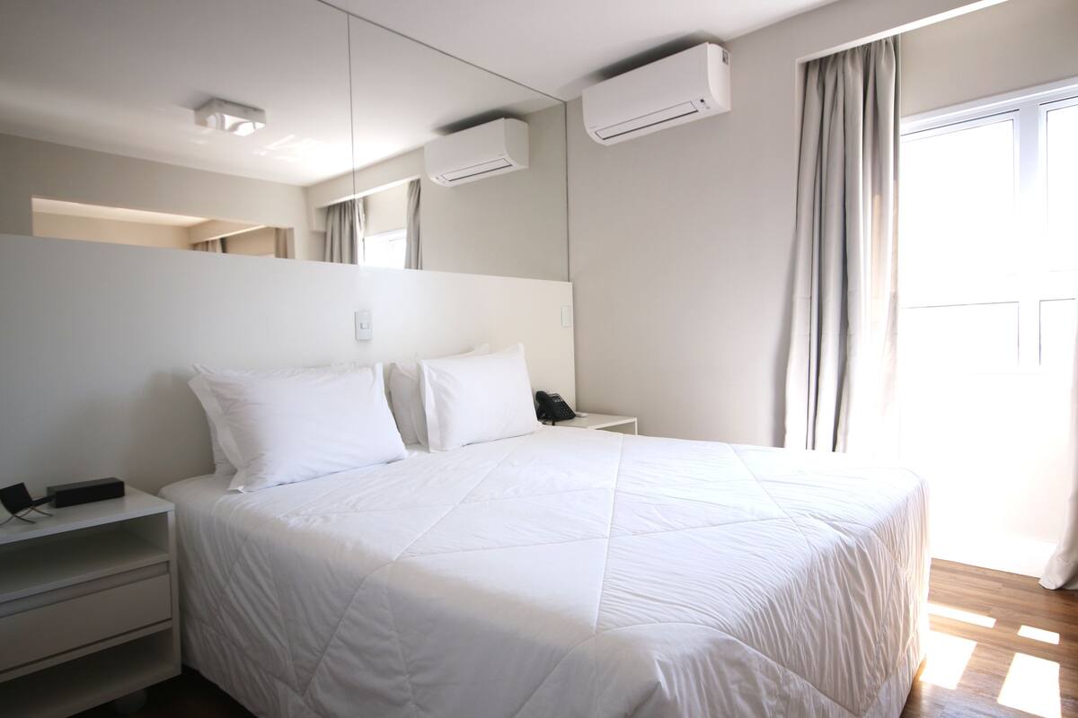 Une chambre d’hôtel moderne avec un grand lit, une table de chevet avec un téléphone et un climatiseur fixé au mur.