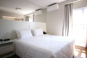 Habitación de hotel moderna con una cama grande, una mesita de noche con teléfono y aire acondicionado instalado en la pared.