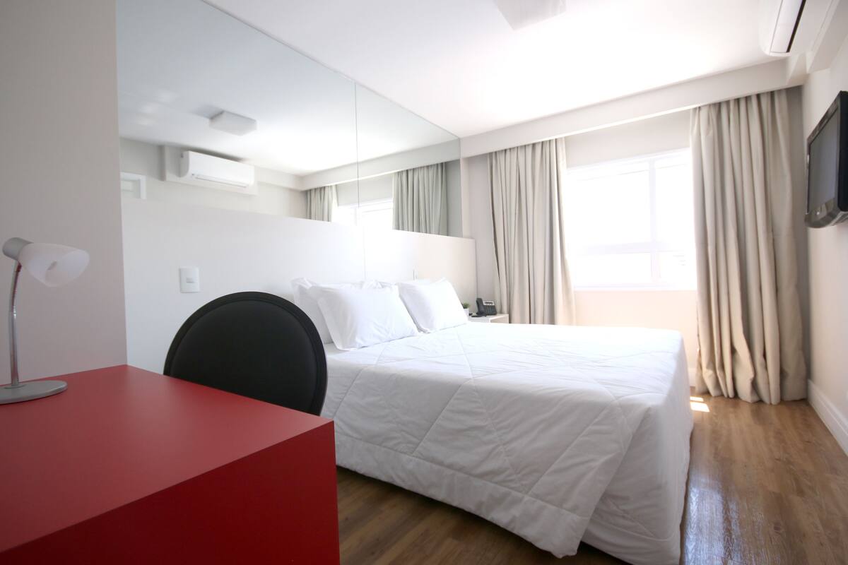 Une chambre d’hôtel avec un lit, un bureau, une chaise, une télévision et une fenêtre avec des rideaux.