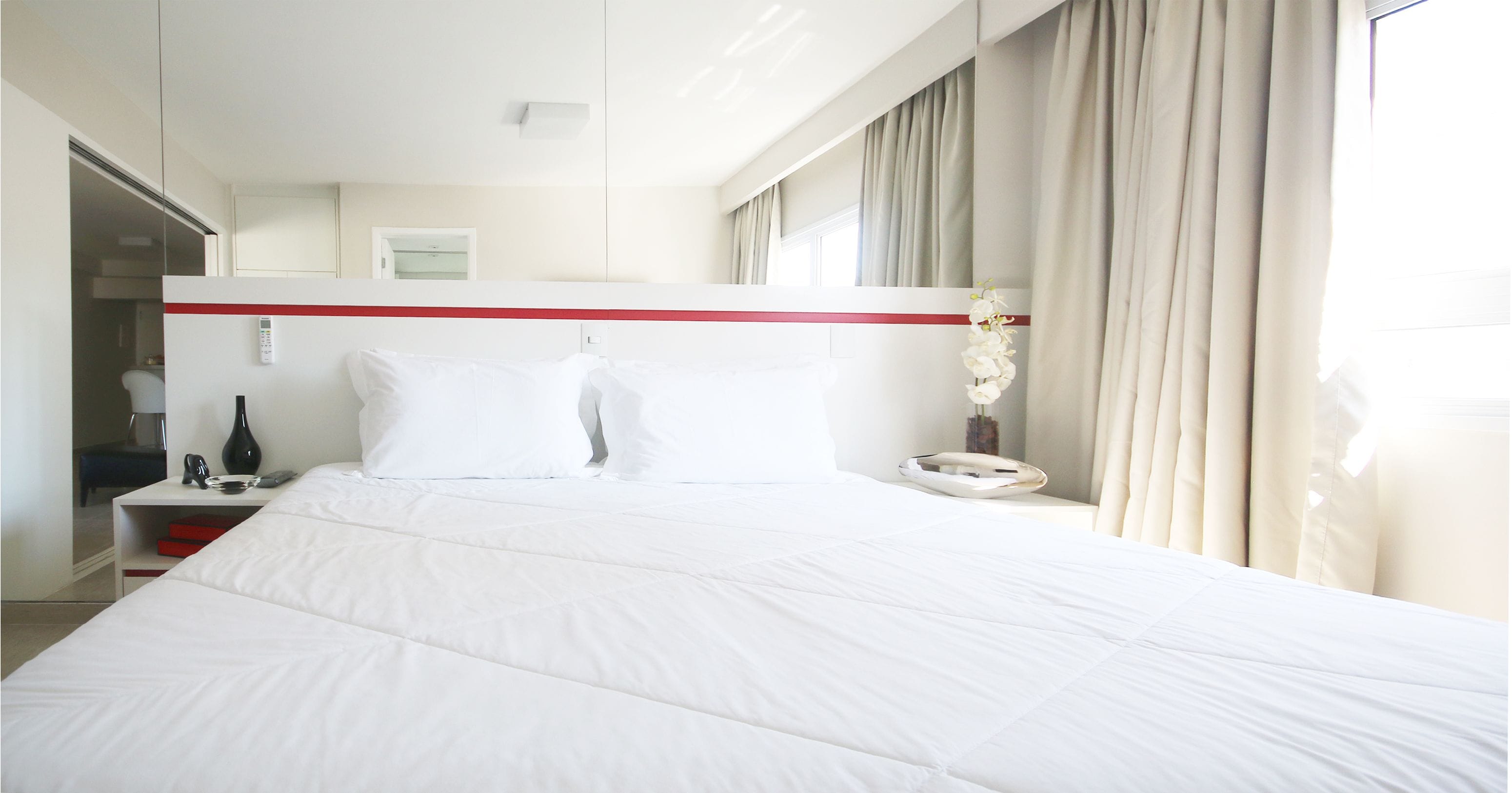 A hotel room with a large bed, a bedside table with a lamp, a telephone, and a mirror above the bed.