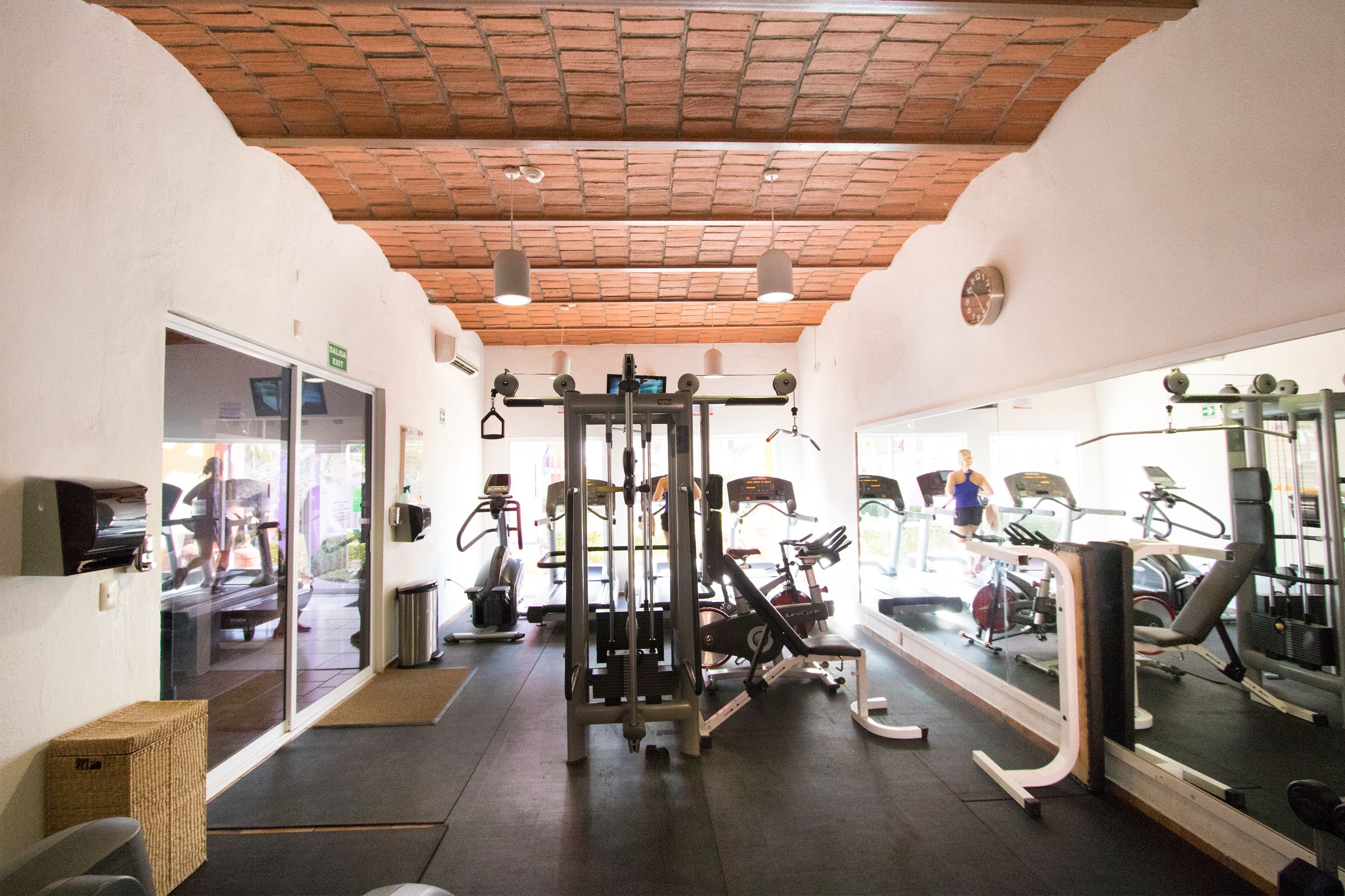 Un gimnasio con diferentes equipos de ejercicio, un espejo grande en la pared y un techo de ladrillo.