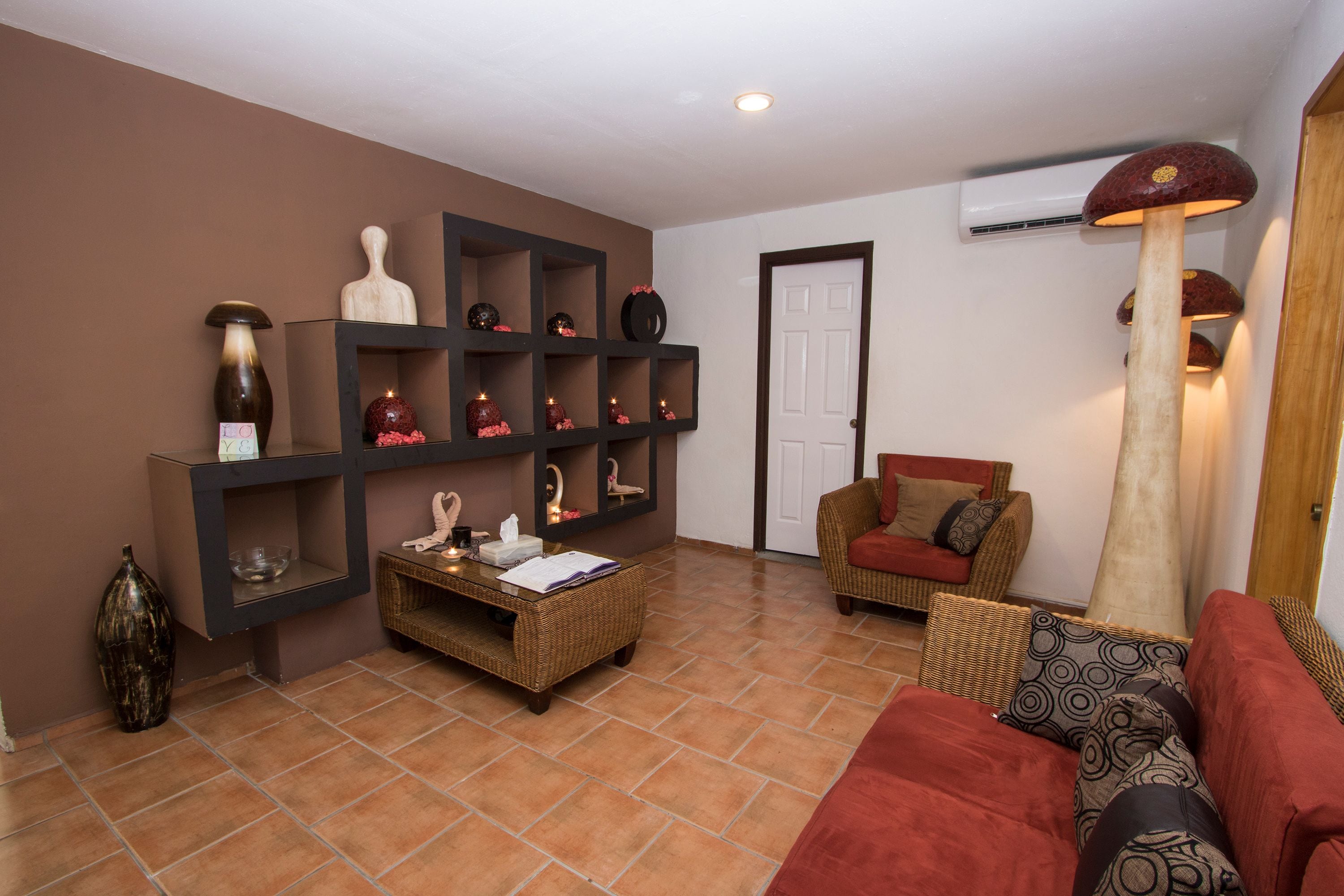 A living room with a brown sofa, a red sofa, a wicker coffee table, and a wall-mounted shelf with decorative items.