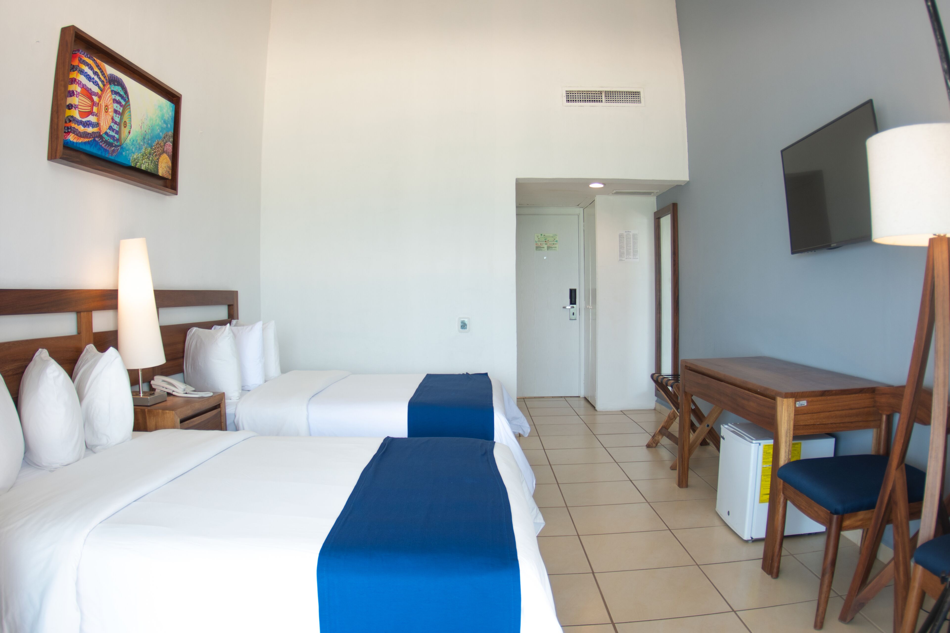 A hotel room with two beds, a desk, a chair, a television, and a painting on the wall.