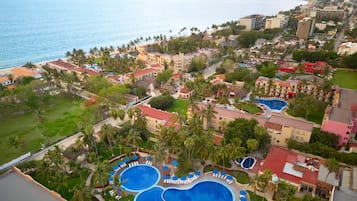 An aerial view of a resort with multiple swimming pools, palm trees, and a beachfront.