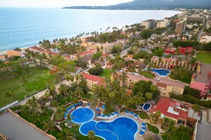 An aerial view of a resort with multiple swimming pools, palm trees, and a beachfront.